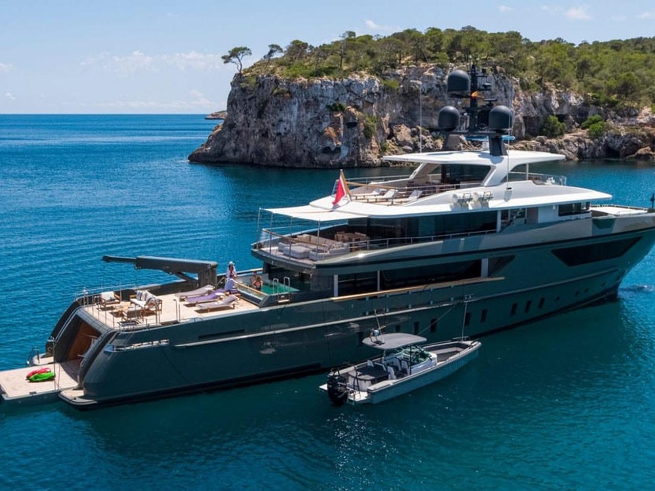 Luxury yacht anchored in turquoise waters with cliffs in the background.
