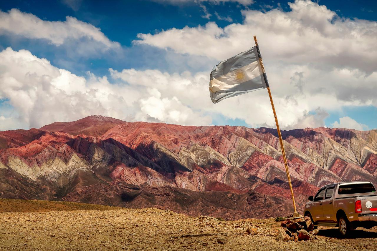 Drapeau argentin flottant avec des montagnes colorées en arrière-plan.