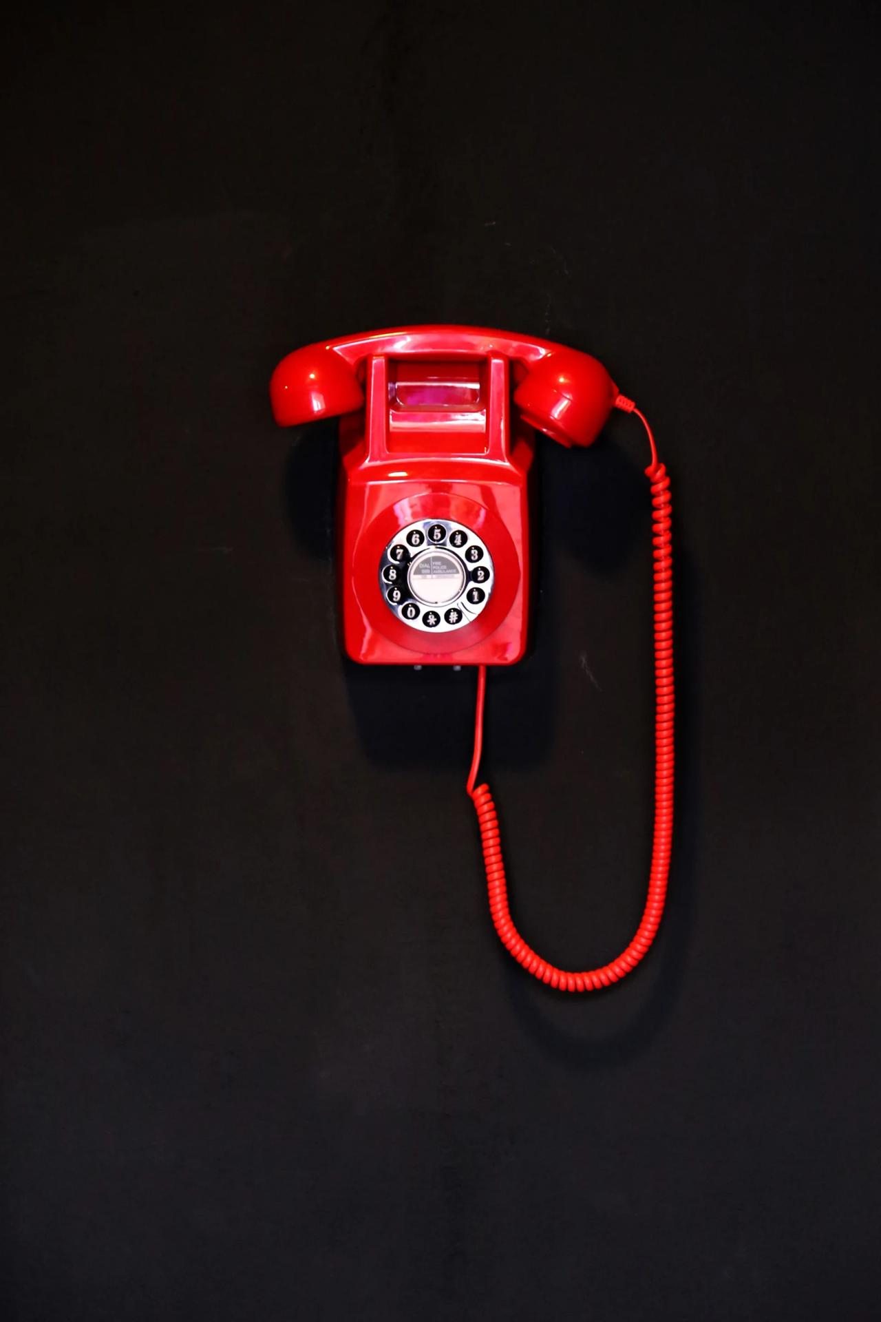 Red vintage rotary telephone on a black wall