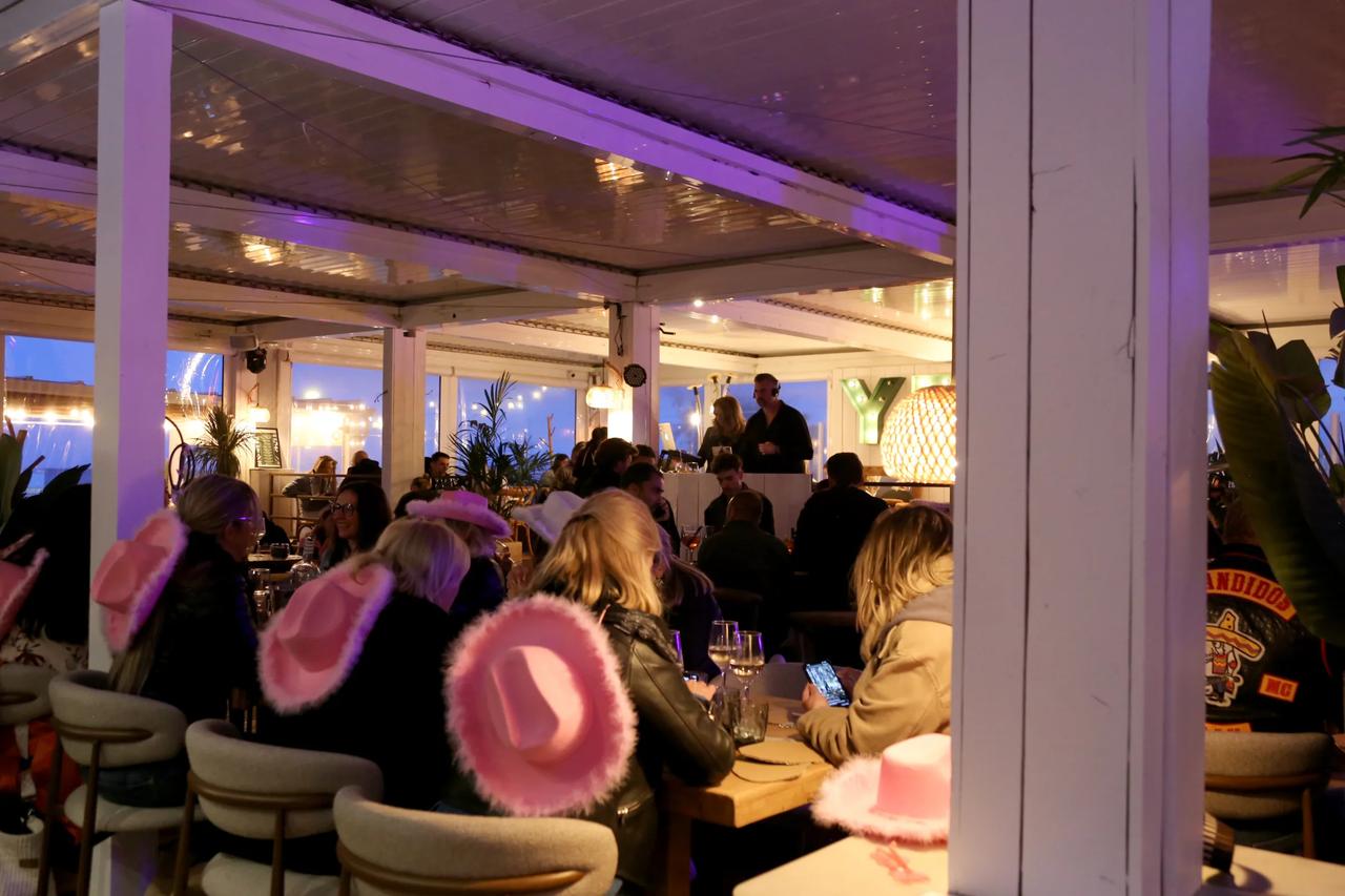Interior view of a lively restaurant with patrons wearing pink hats.