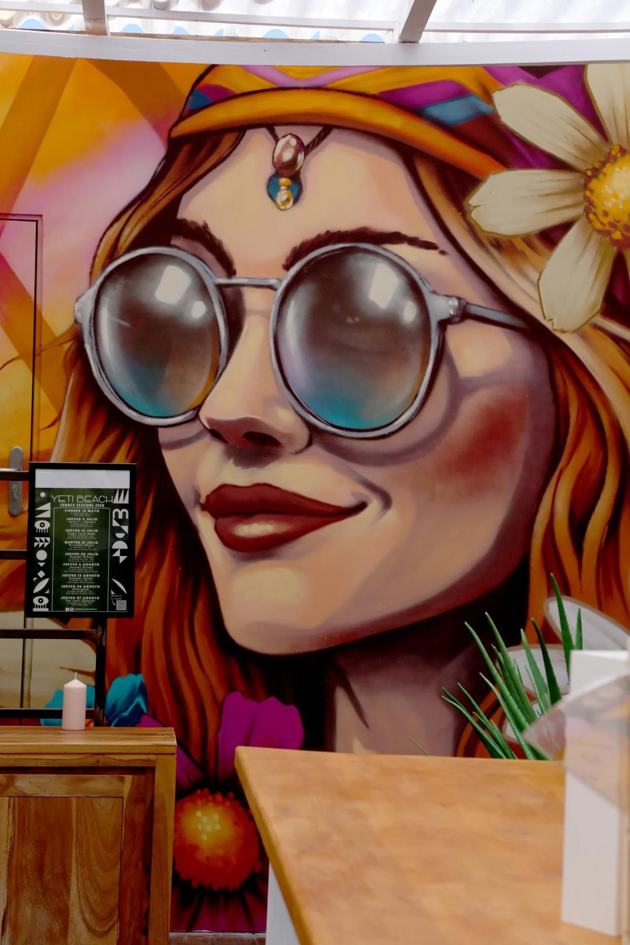Colorful mural of a woman with sunglasses and flower in her hair.