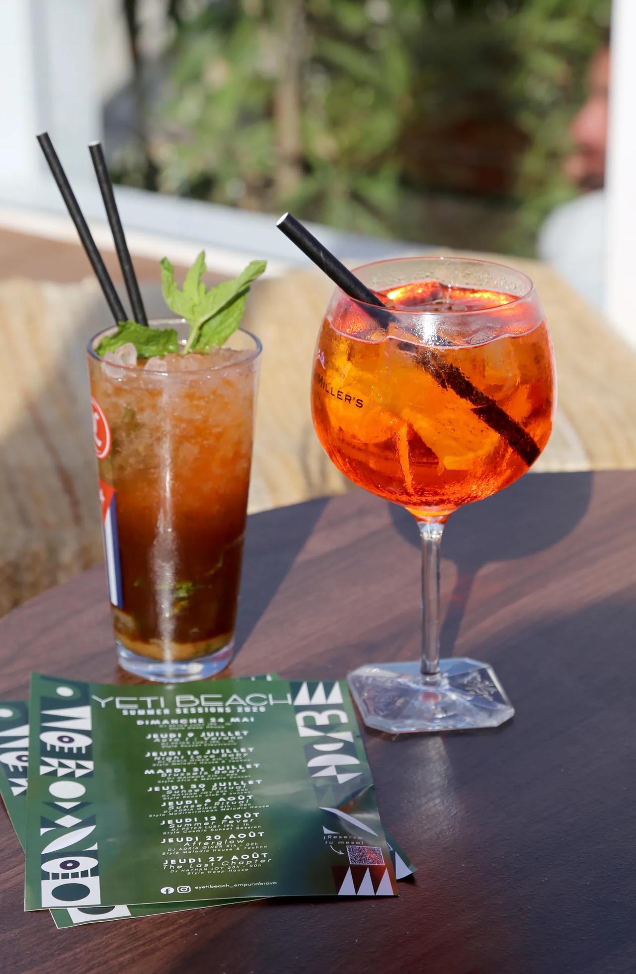 Two cocktails on a wooden table with a menu in the foreground.