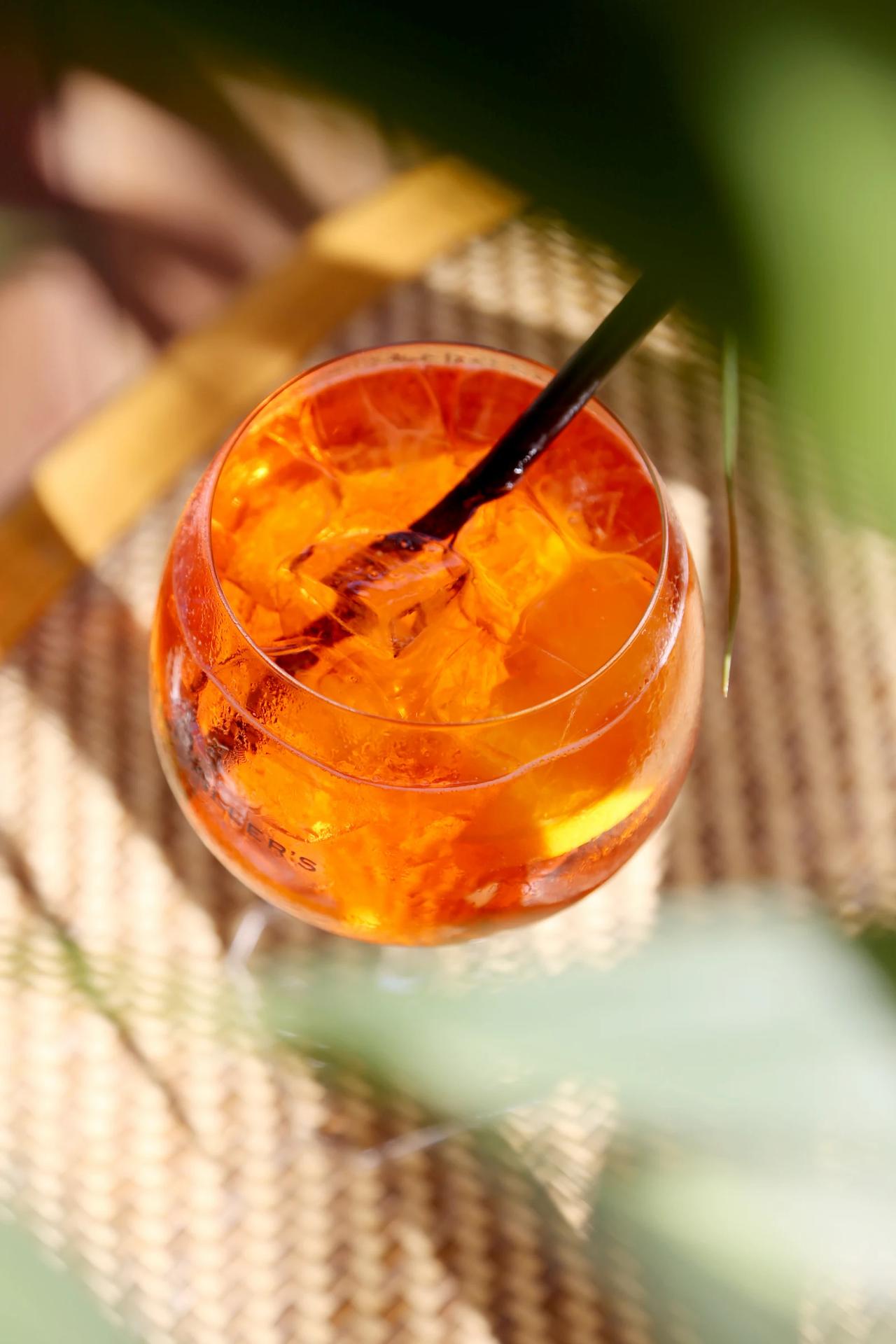 A close-up of a vibrant orange cocktail in a glass with ice.