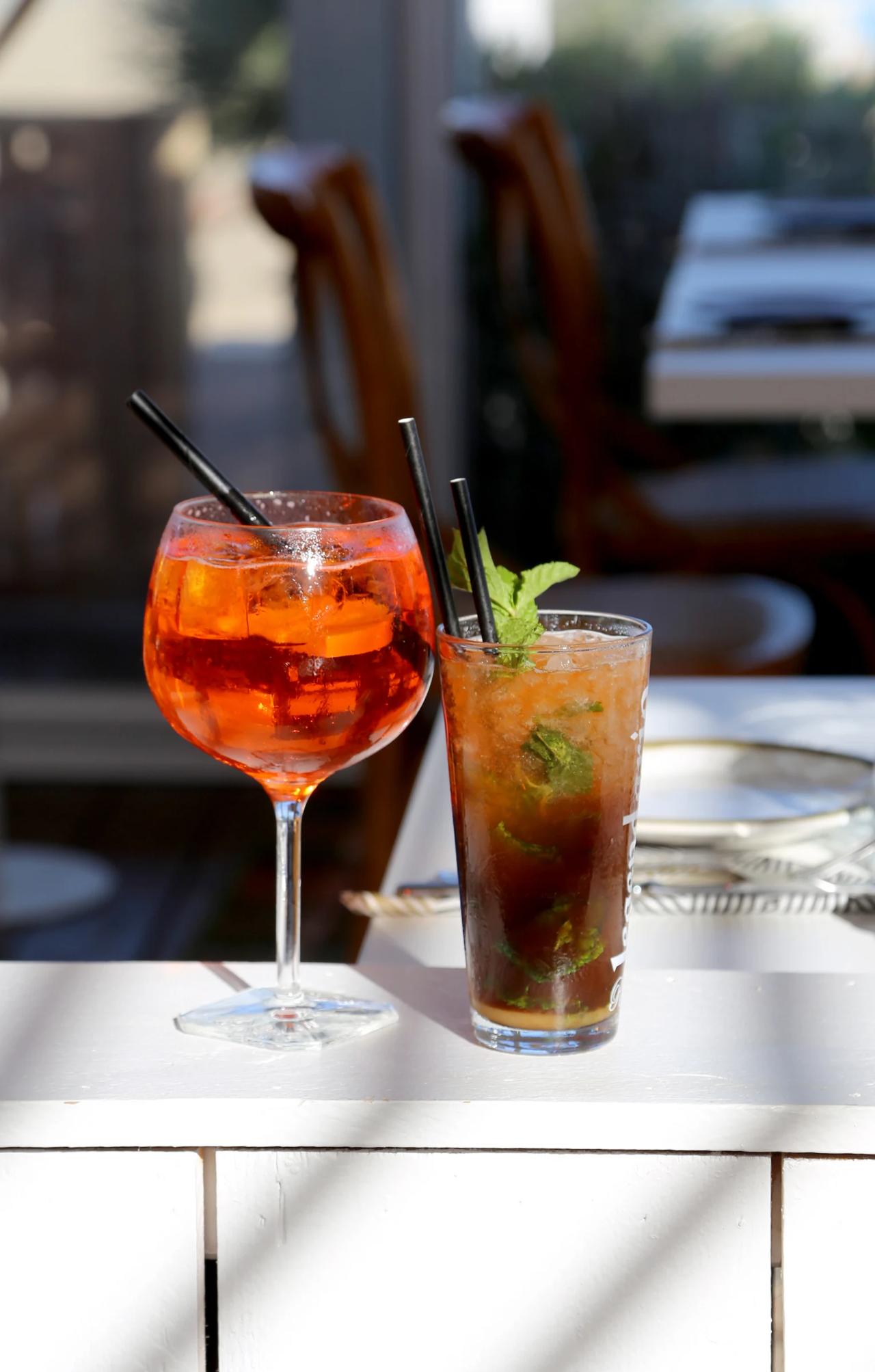 Two cocktails on a table, one in a large glass and one in a tall glass.