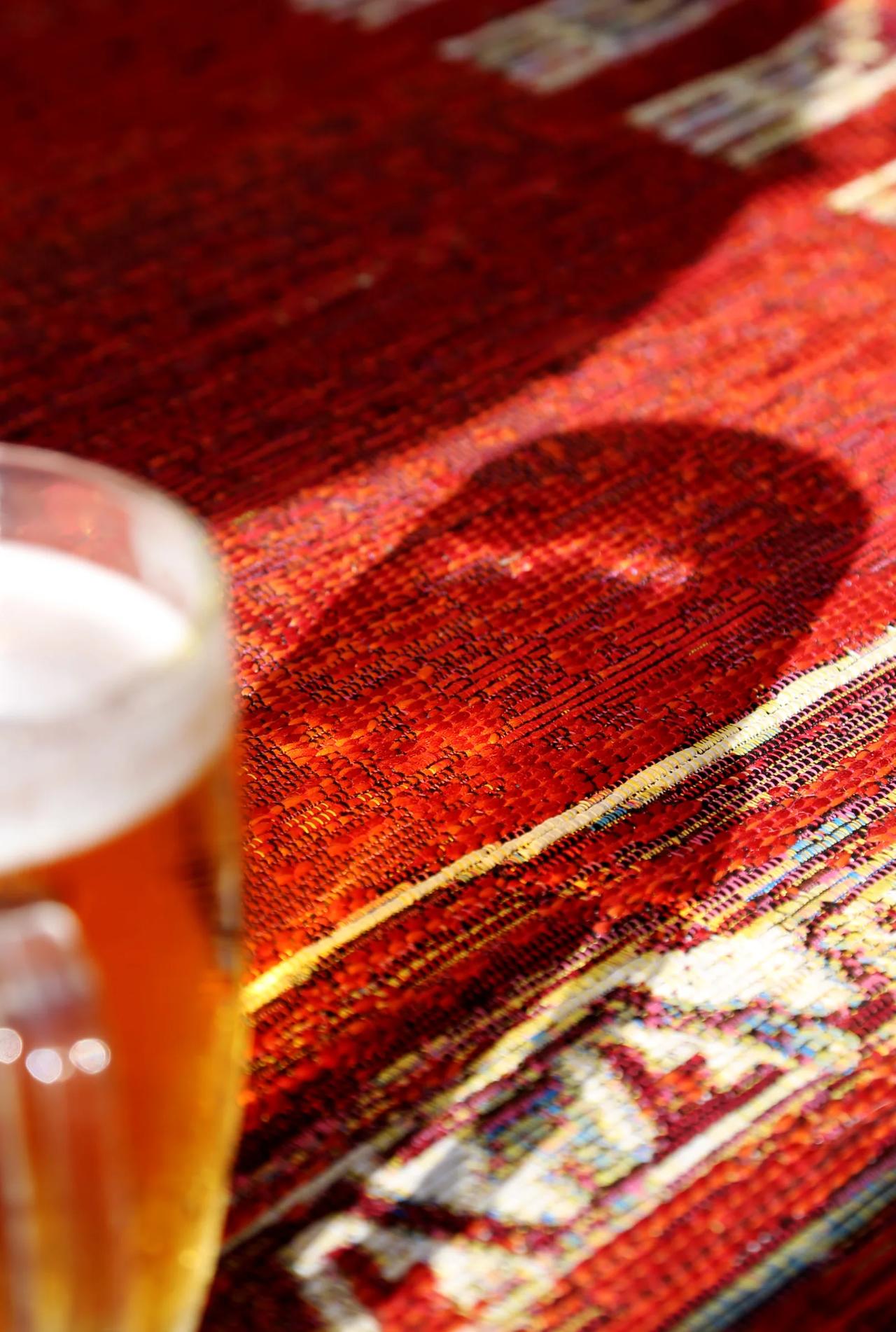 Close-up of a beer glass on a textured red surface.