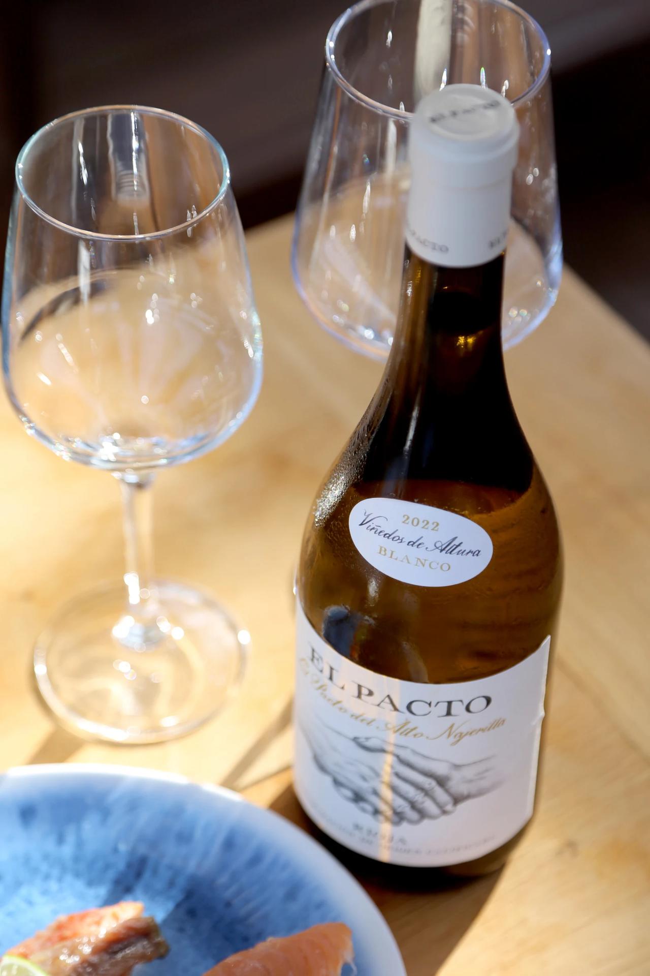 Bottle of El Pacto white wine with glasses on a wooden table.