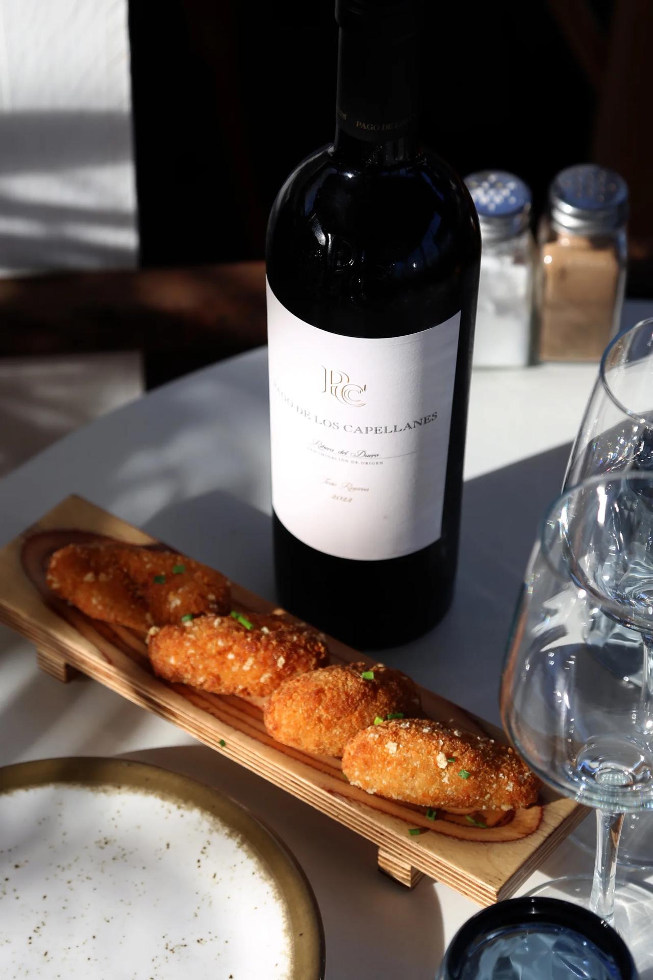 Croquettes on a wooden platter with a bottle of red wine
