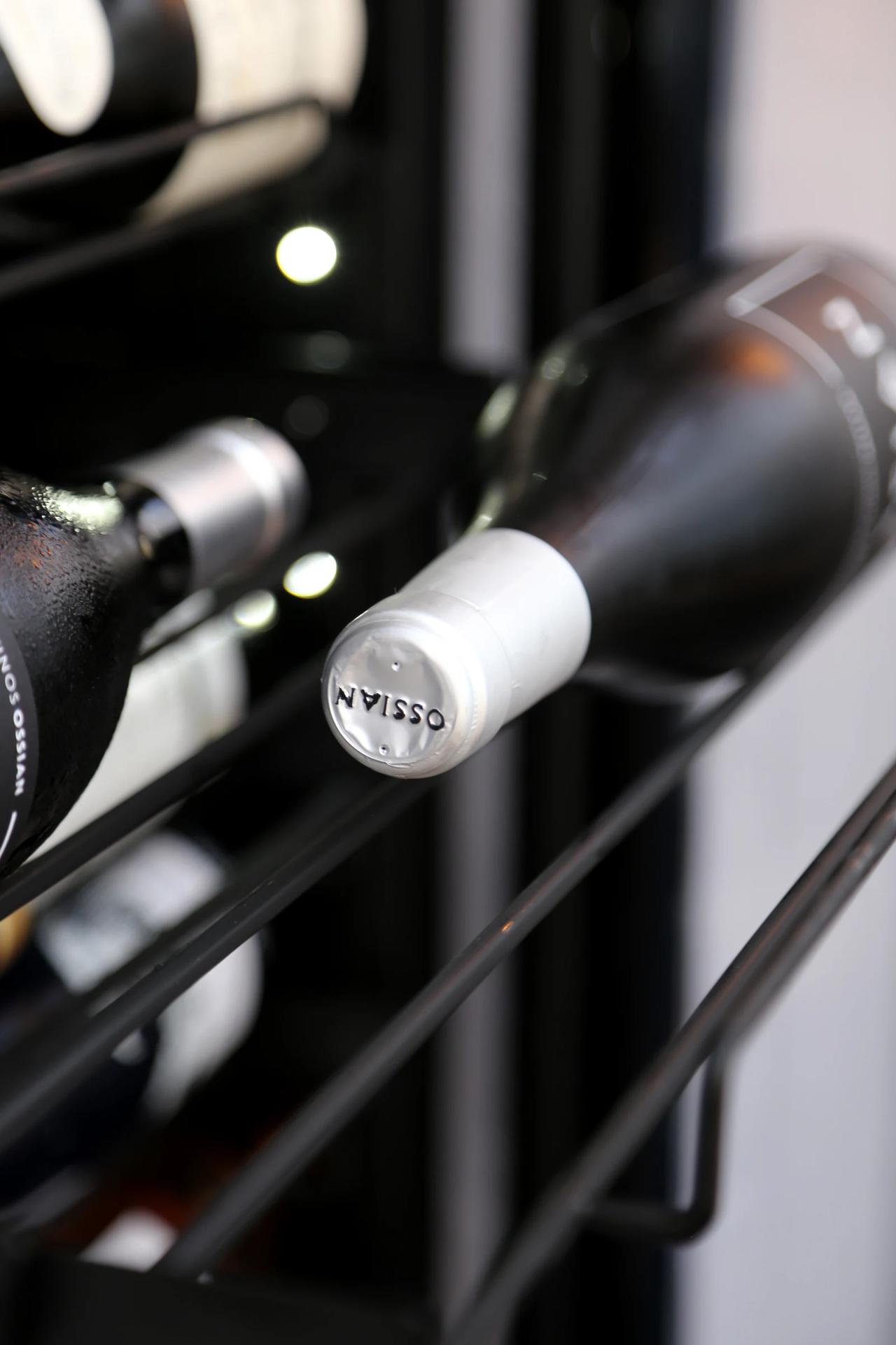 Close-up of a wine bottle with a white cap on a rack.