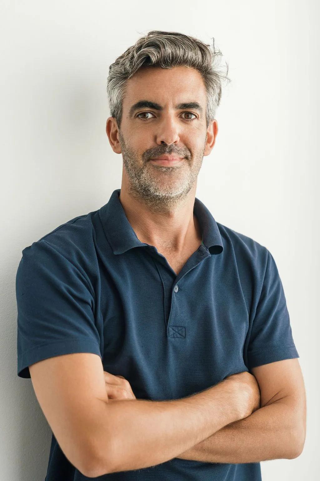 Man with gray hair in a navy polo shirt, arms crossed