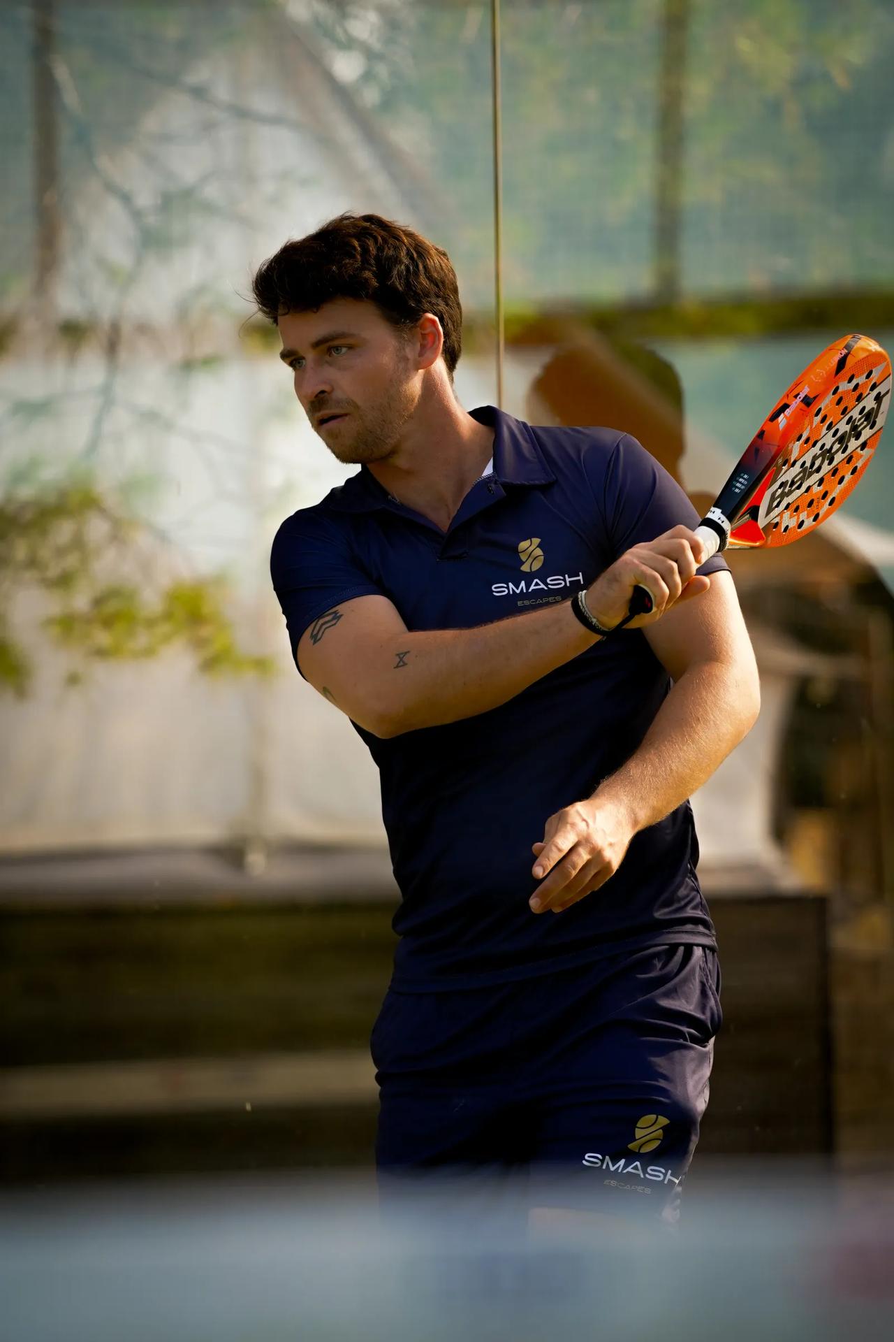 Man playing padel tennis, wearing a Smash Escapes shirt.