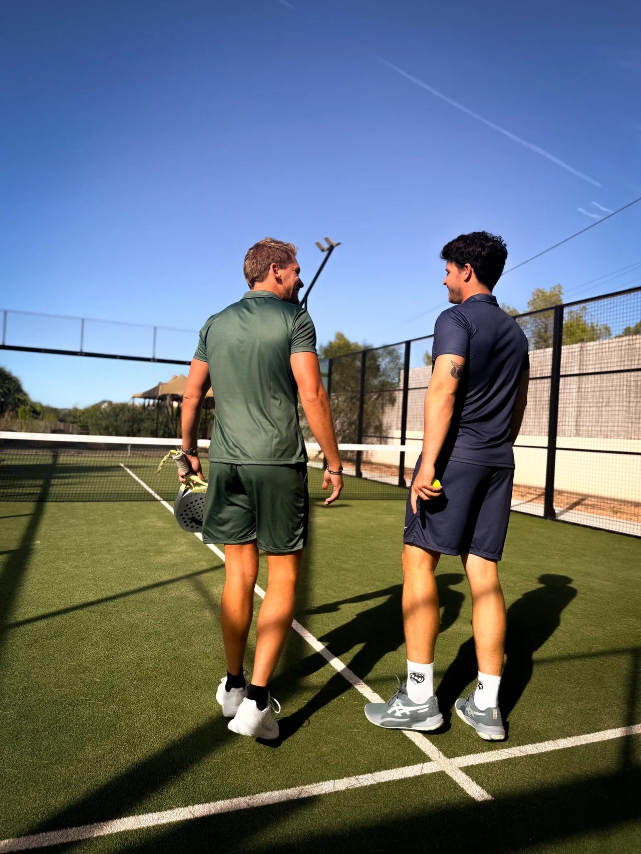 Two tennis players discussing on a court under a clear blue sky.