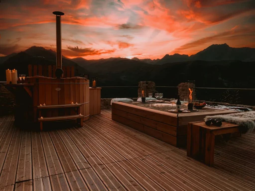 Terrasse d'un chalet avec jacuzzi et vue sur les montagnes au coucher du soleil.