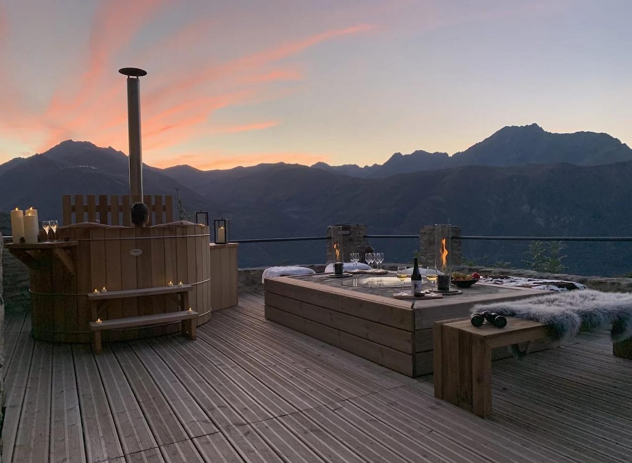 Terrasse d'un chalet avec un jacuzzi et une vue sur les montagnes au coucher du soleil.