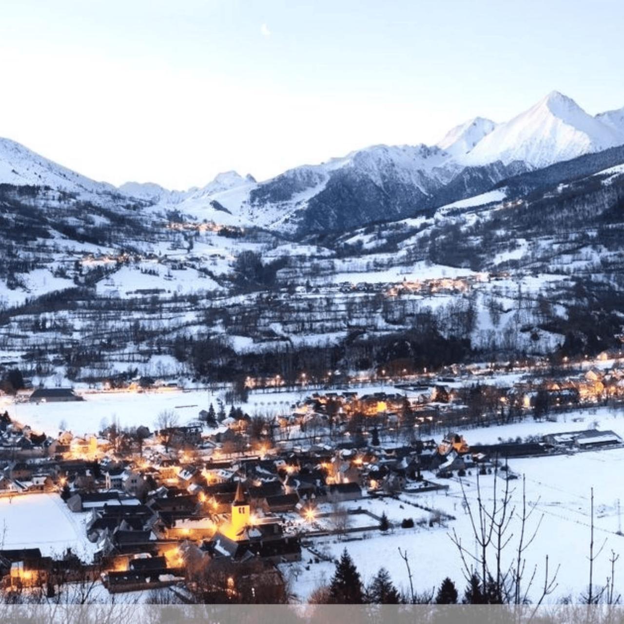 Vue panoramique d'un village enneigé avec des montagnes en arrière-plan.