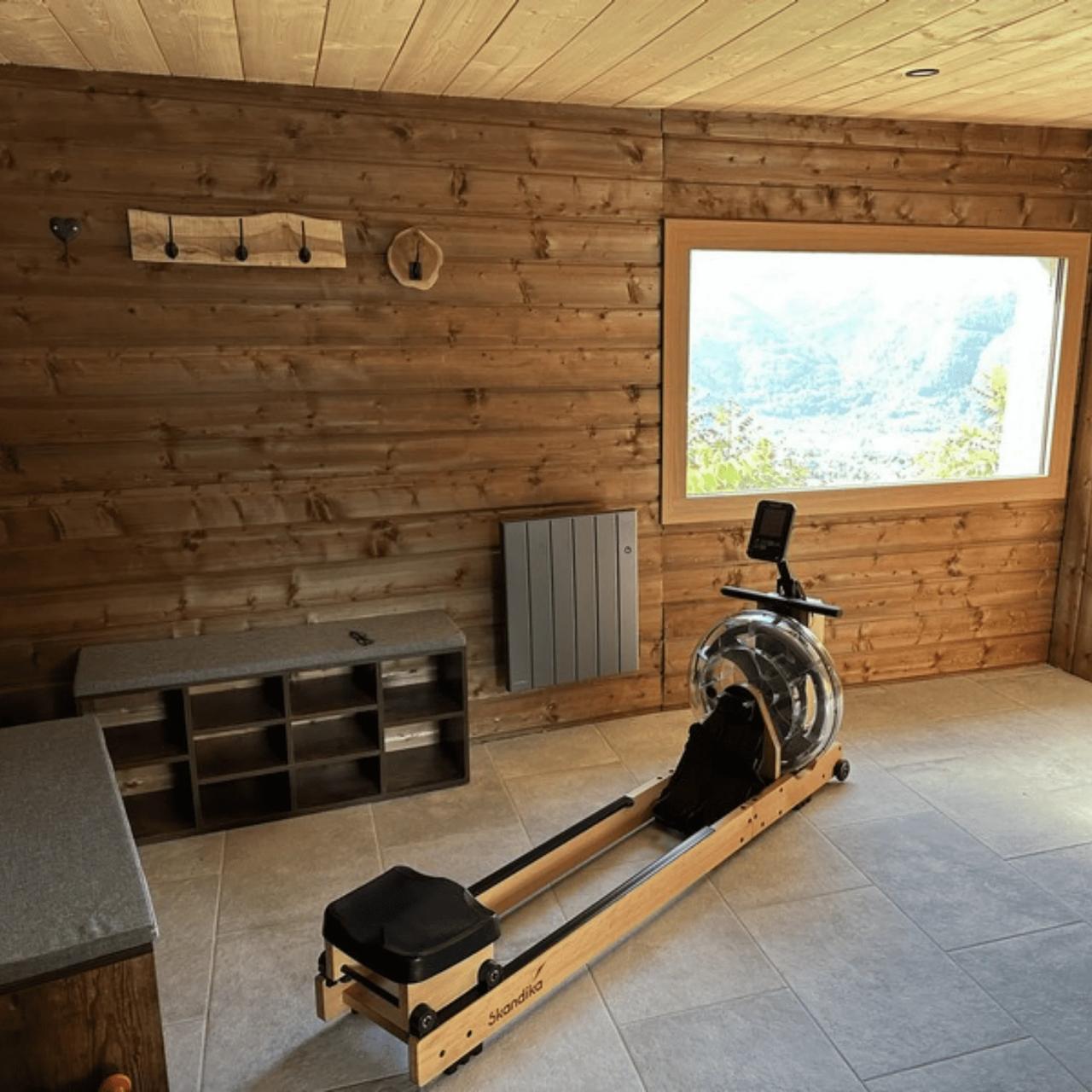 Salle d'exercice avec un rameur en bois et vue sur la montagne.