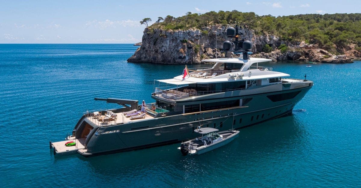 Luxury yacht anchored in turquoise waters with cliffs in the background.