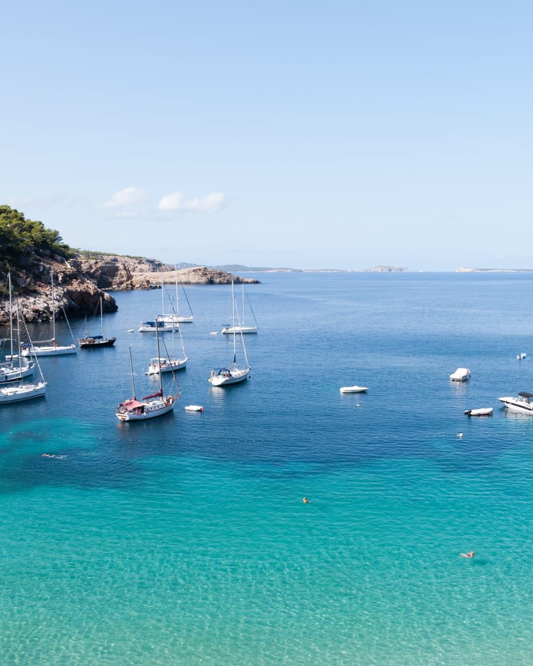 Sailboats anchored in a calm turquoise bay with clear skies.