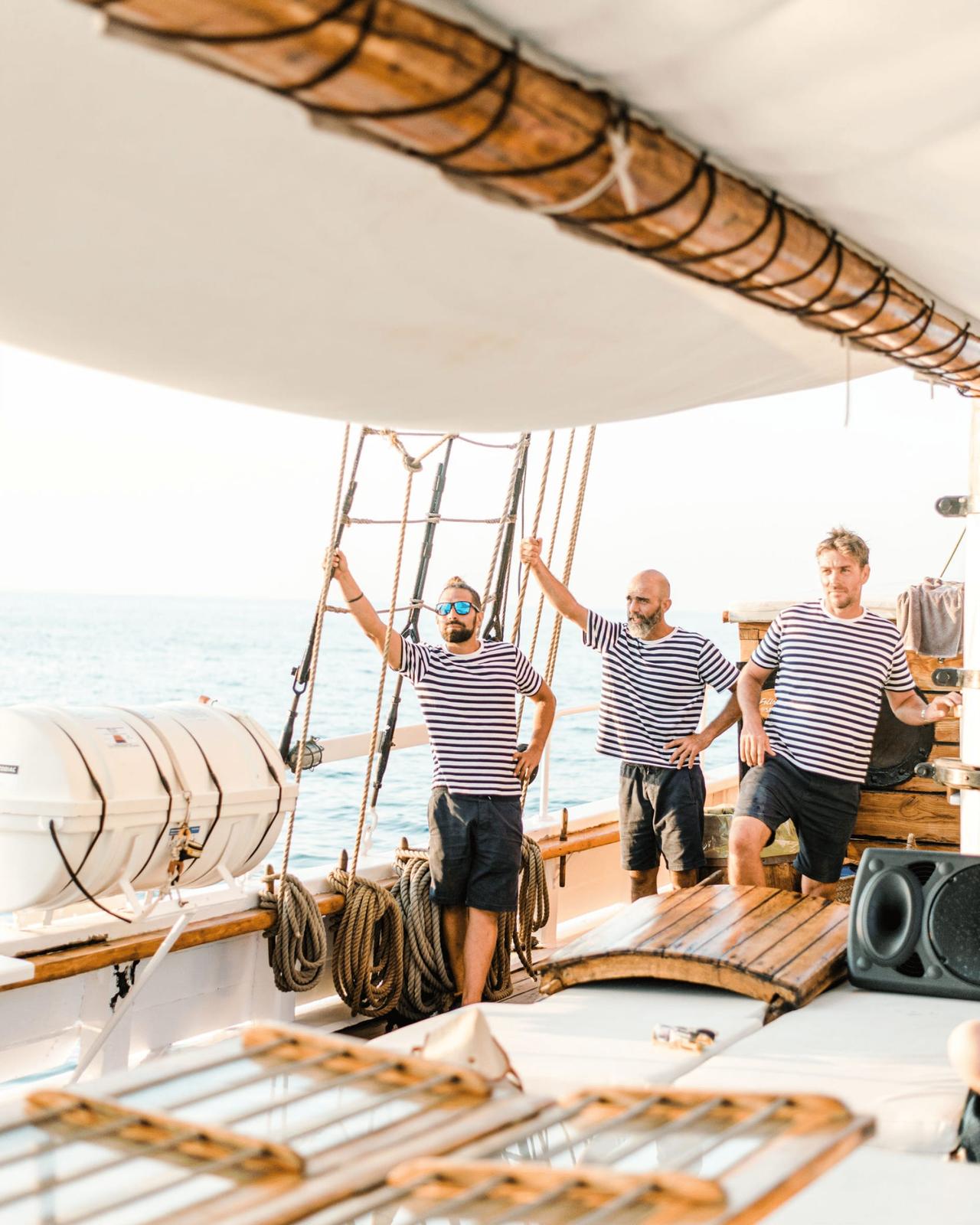 Three men in striped shirts on a boat deck by the sea.