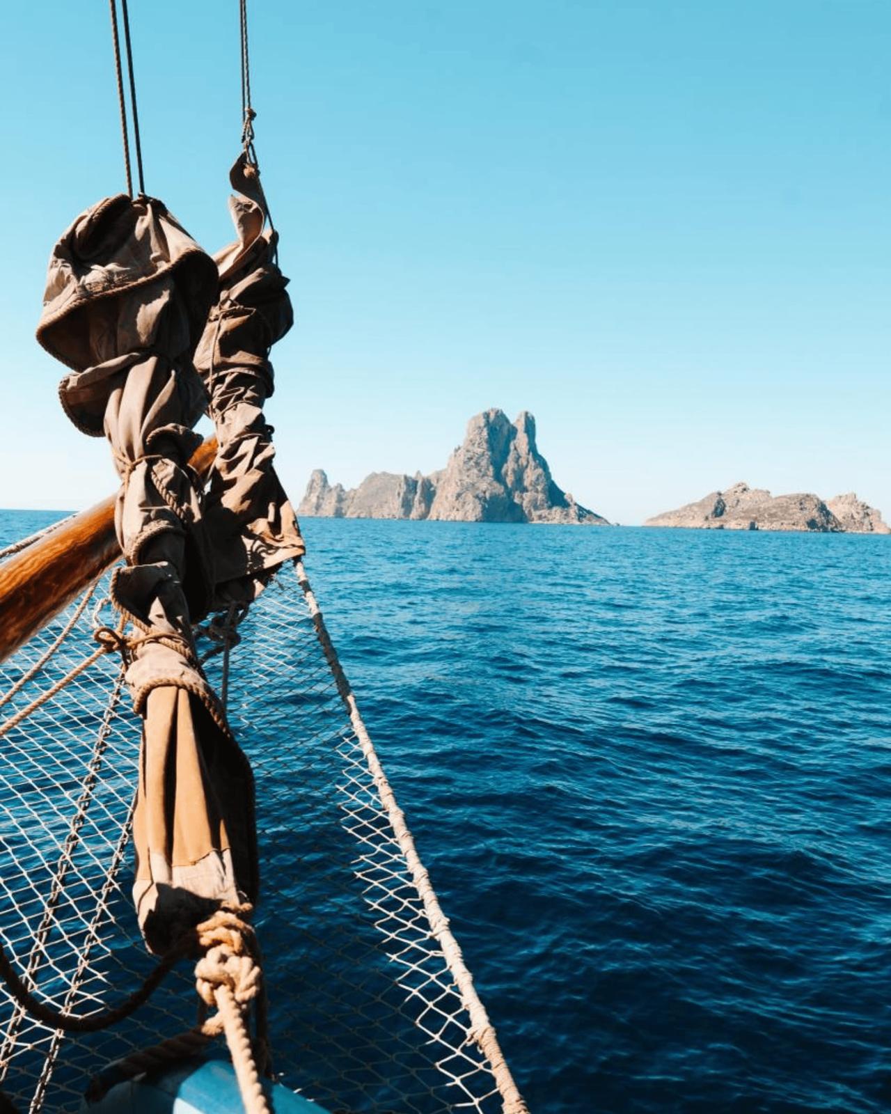 View from a boat showing a rocky island in the distance against a clear blue sky.