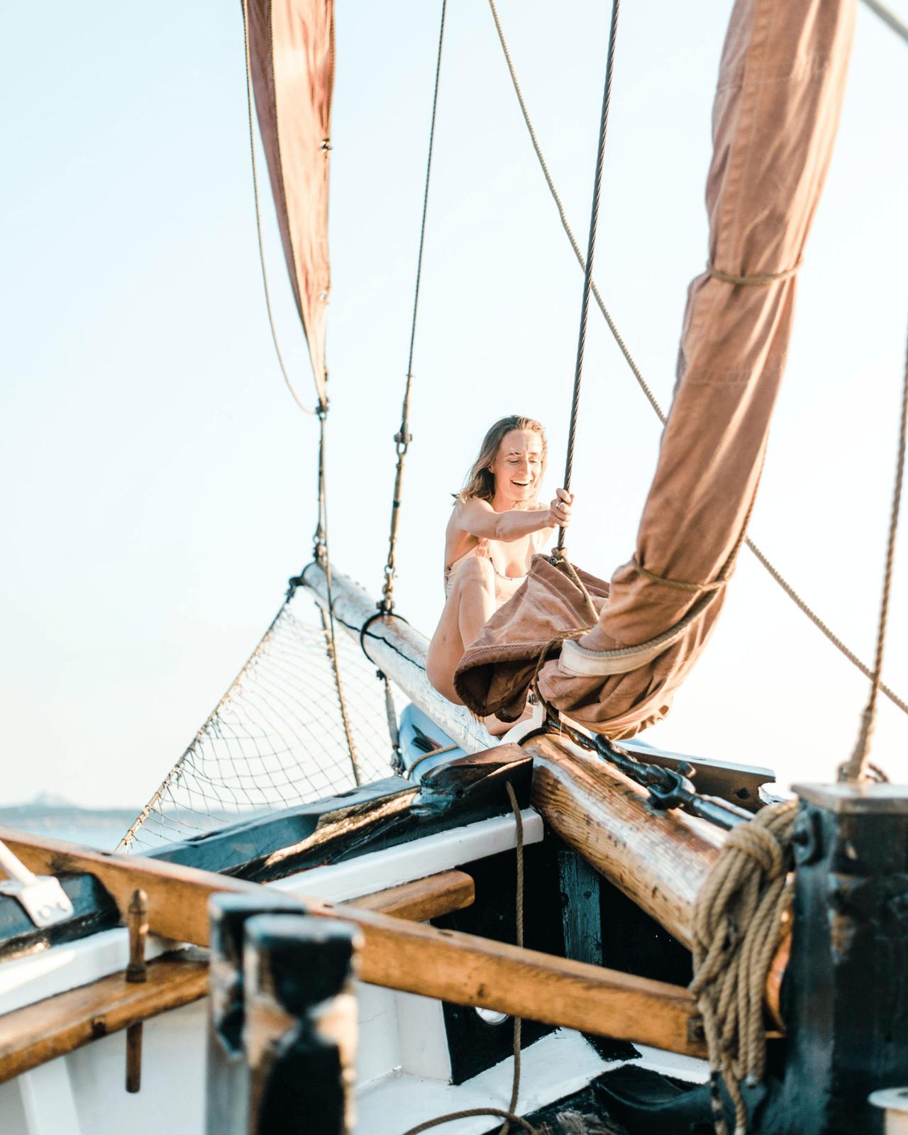 A person adjusting sails on a boat under clear skies.