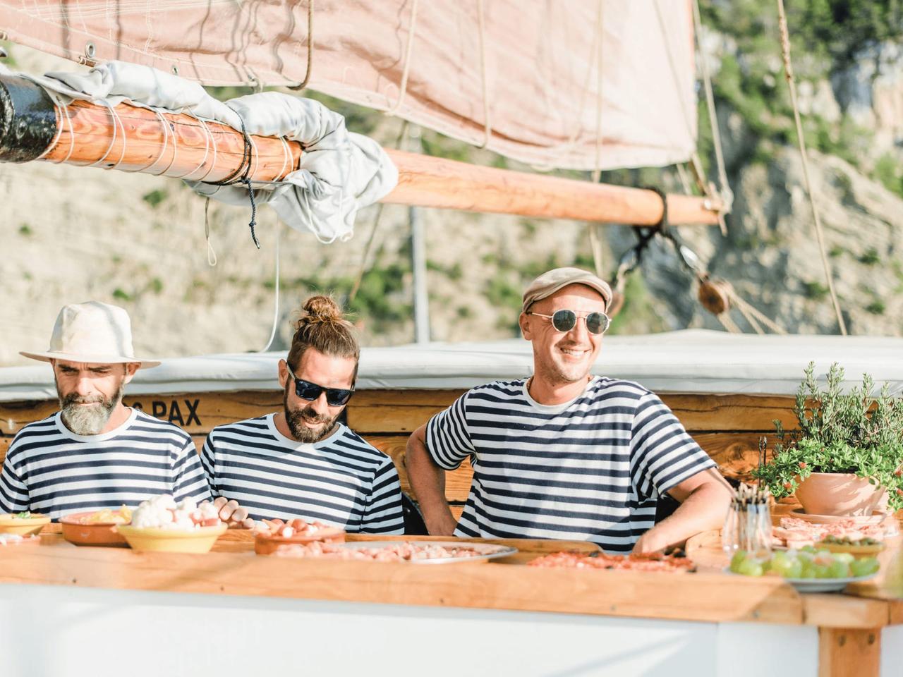 Three men in striped shirts serving food on a boat.