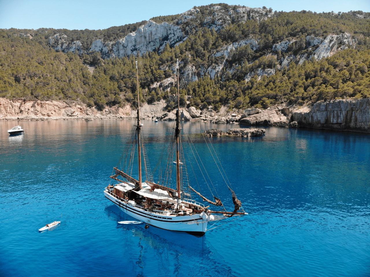 Sailing boat anchored in a clear blue bay surrounded by cliffs and greenery.