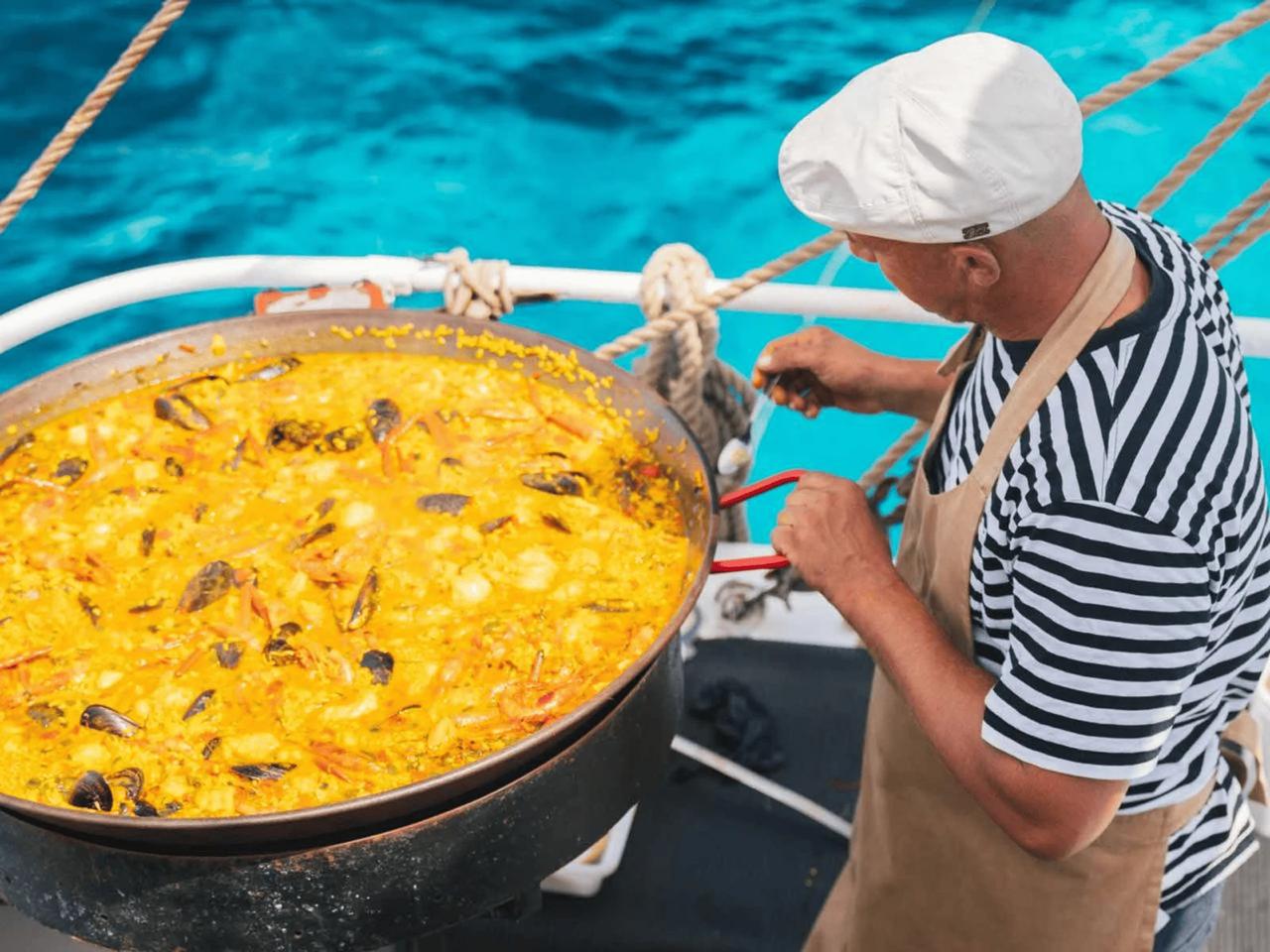 A chef preparing a large paella on a boat with blue water in the background.