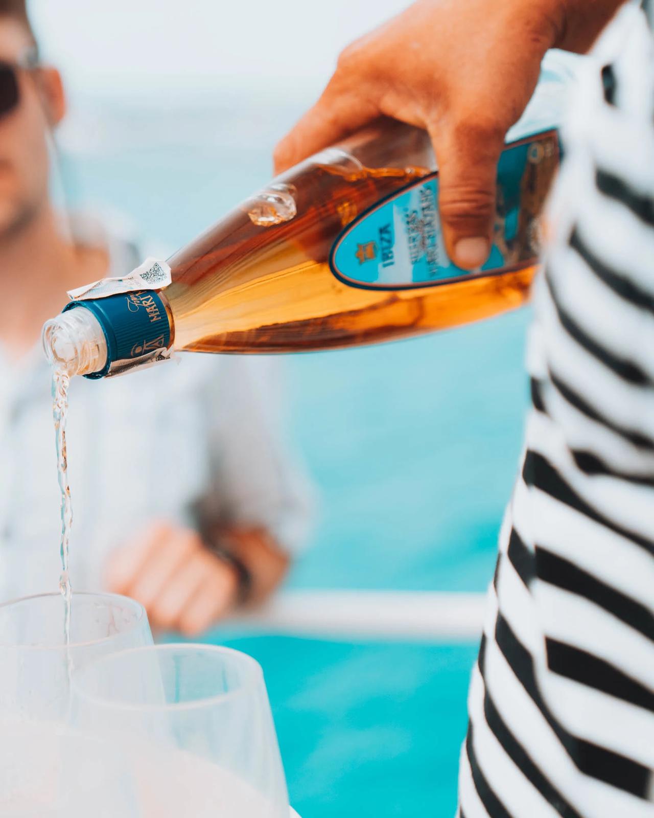 A hand pouring a drink from a bottle into glasses on a boat.