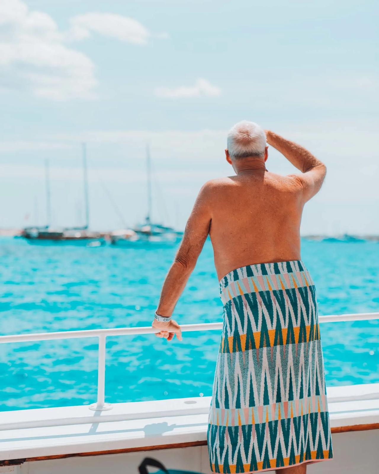 Man in a patterned towel looking out at the sea from a boat.
