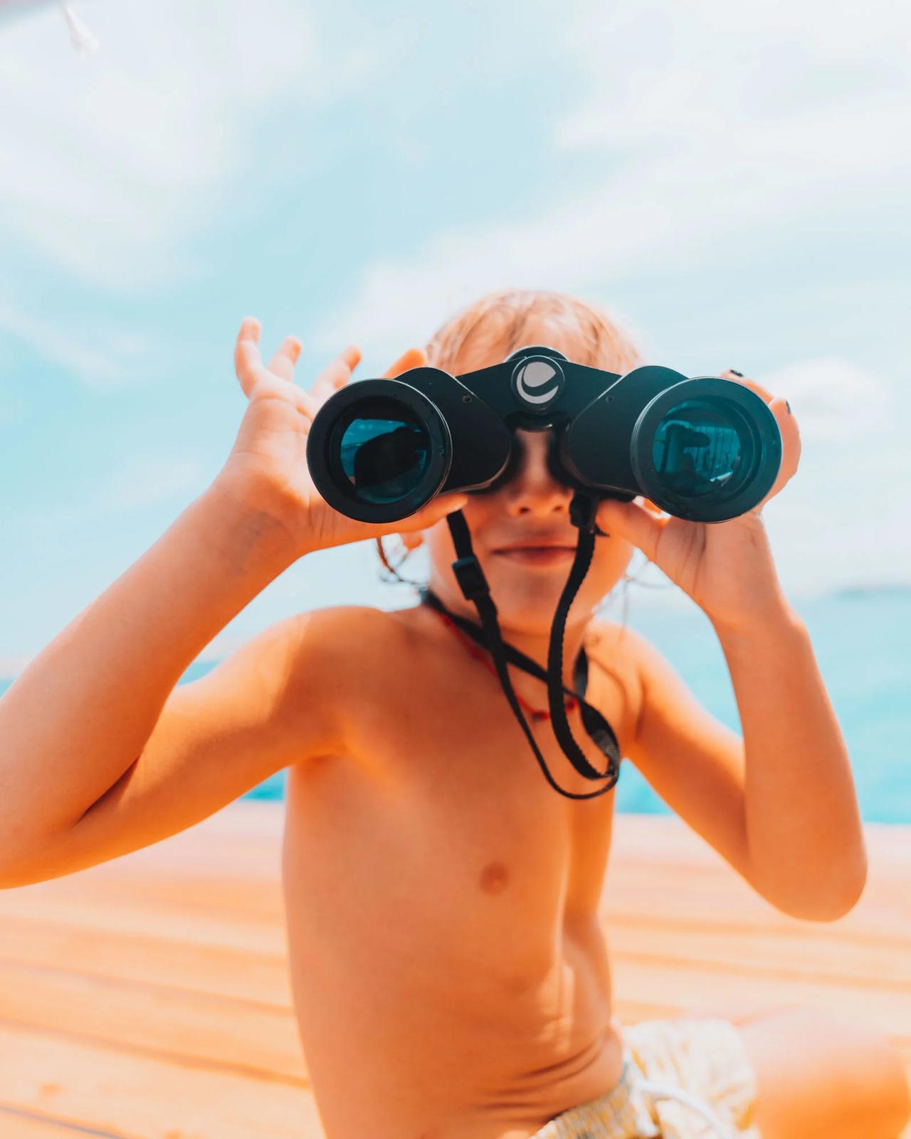 Child holding binoculars on a boat, looking out at the sea.