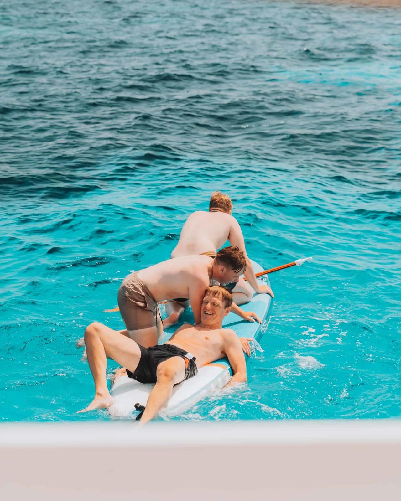 Three young men enjoying a paddleboard on clear turquoise water.