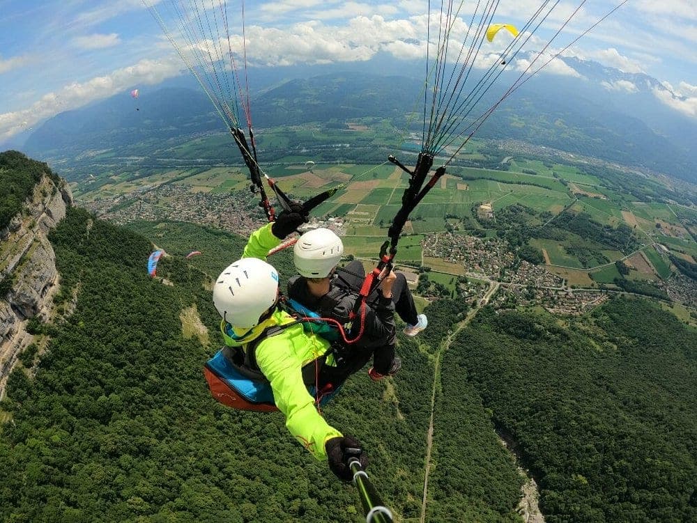 Deux personnes en parapente survolant un paysage verdoyant.