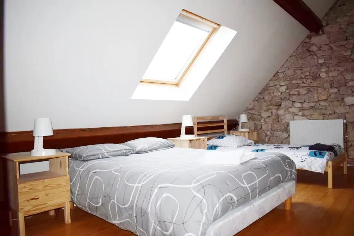 Chambre d'angle avec lit double et lit simple sous un toit en pente.