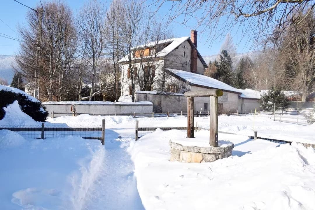 Un puits en pierre entouré de neige avec une maison en arrière-plan.