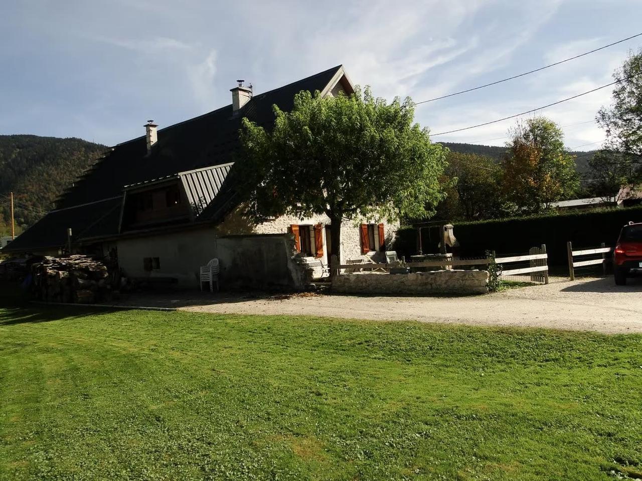 Maison en pierre avec un grand jardin et des montagnes en arrière-plan.