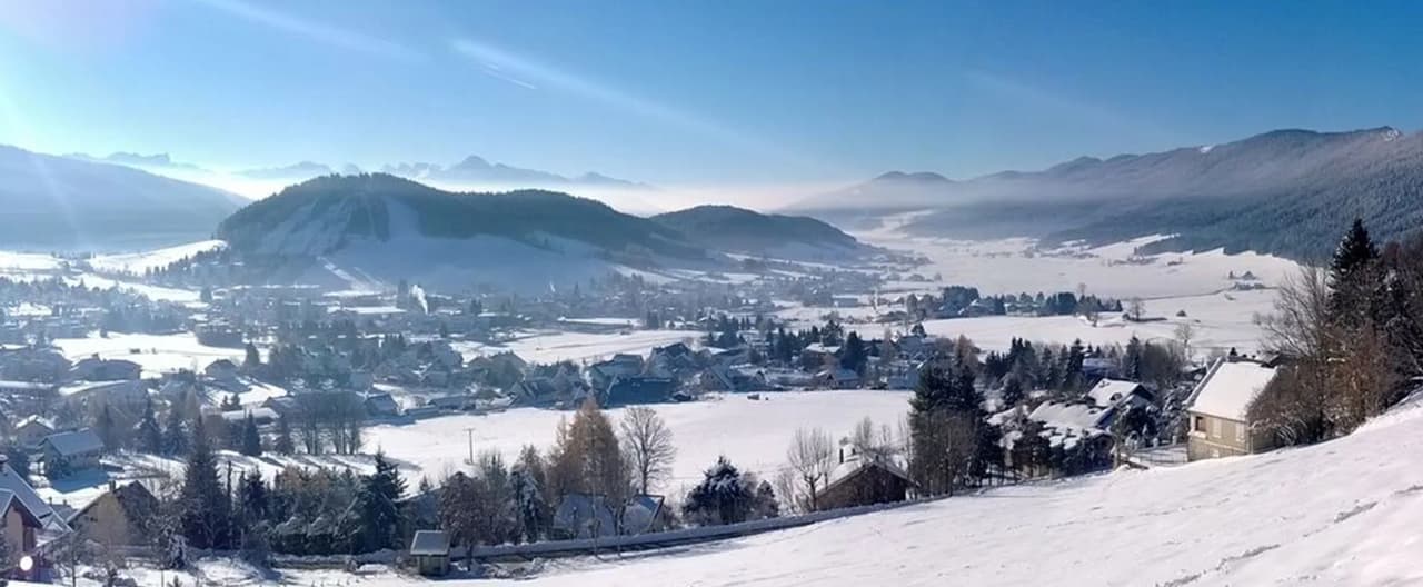 Vue panoramique d'Autrans sous la neige avec montagnes en arrière-plan.