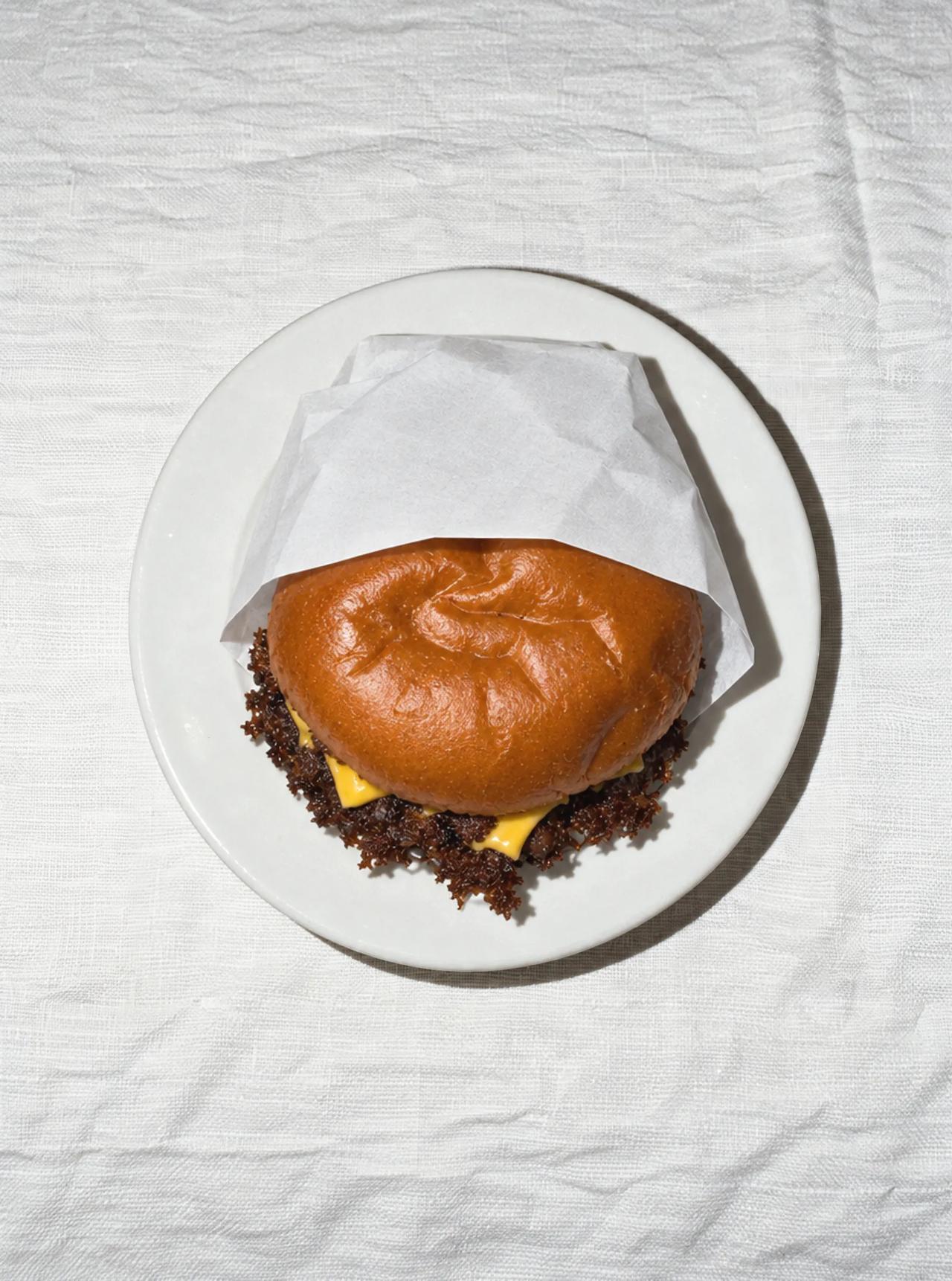 Un hamburger sur une assiette blanche avec un pain brun.